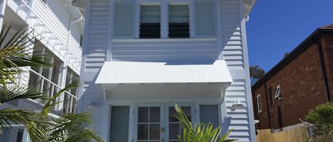 Exterior of two storey beach cottage. Louvred windows for sea breeze.
