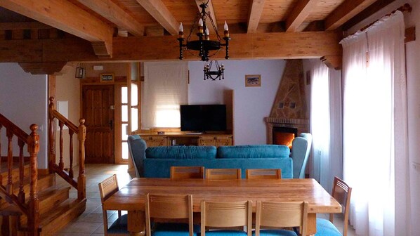 Salón comedor con TV, sofás, chimenea, libros y juegos y mesa para 8 comensales.