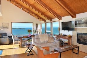 A large living room has a dining table surrounded by windows with a beautiful views.