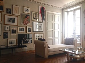 Drawing/living room with light pouring in from two windows with shutters.