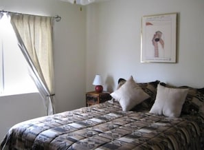 This second bedroom has a view of the yard and also a nightstand and chair.