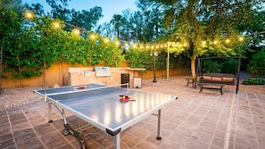 Ping pong table near the outdoor kitchen w/ BBQ, seating, & string lights