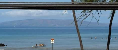 Outrigger canoes paddle away while surfers wait for waves in the distance