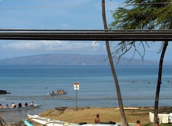 Outrigger canoes paddle away while surfers wait for waves in the distance