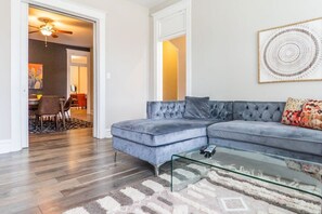 A tufted carpet and mod glass coffee table complement the room’s turn-of-the-century white door frames and trim.