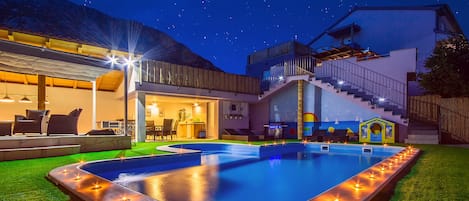 The night look of a beautiful pool, lounge and dining area with outdoor kitchen