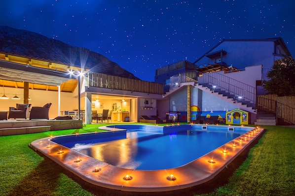 The night look of a beautiful pool, lounge and dining area with outdoor kitchen