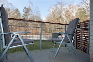 A balcony area with a comfortable chair and small table, ideal for relaxing outdoors. The view includes a natural green landscape.