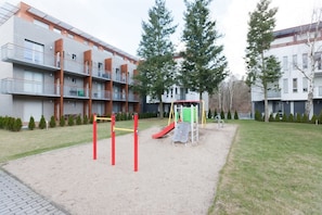 An outdoor area with a playground surrounded by greenery and trees. The setup is simple and suitable for children.