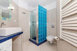 A modern bathroom with blue-tinted glass blocks separating the shower area, featuring white tiles and a single sink.