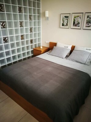 A cozy bedroom with a dark gray bedspread on a double bed, soft lighting, and a patterned accent wall behind the bed.