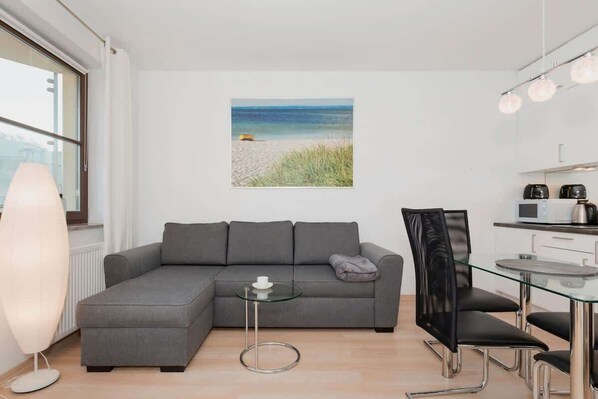Elegant living room with grey double sofa bed, stylish coffee table, and glass dining table.