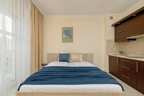Close-up of the double bed on which the navy blue bedspread lies. To the right is the kitchenette.