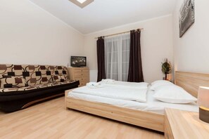 Comfortable and spacious living area with sofa, double bed, television, cabinets and stylish dark brown curtains.