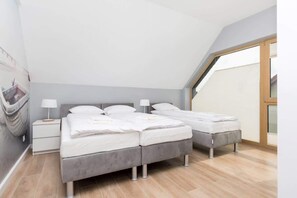 A cozy bedroom with single beds, light gray bedding, wooden floors, and a soft, warm atmosphere created by slanted ceilings and modern decor.