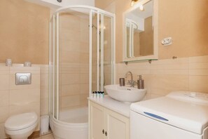 A modern bathroom with a shower stall, toilet, and a wash basin. The neutral tile walls and clean lines make the space look elegant and fresh.