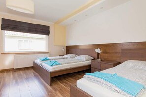Bedroom with two double beds. One of them stands closer to a large window through which plenty of natural light enters. 