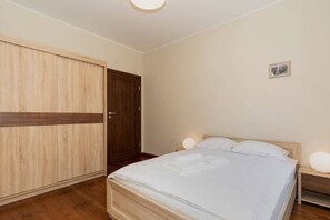 A spacious bedroom with a large wardrobe made of dark wood and a comfortable double bed with white linens. The room has a calm, neutral color palette.