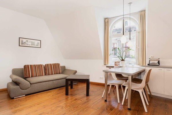  A cozy living room with a light brown sofa, a small wooden coffee table, and a window that lets in natural light. The room has sloped ceilings, adding character to the space.