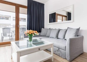 A soft grey sofa over which hangs a rectangular mirror allows you to relax and unwind at the charming coffee table. 