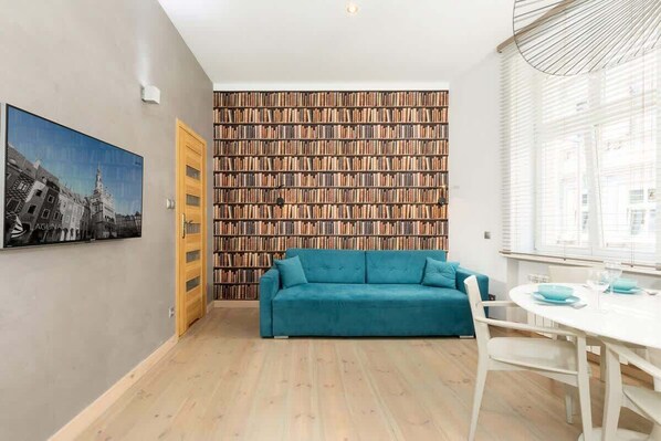 A modern living room featuring a vibrant teal sofa and a wooden coffee table. The wall behind the sofa has a striking patterned design, adding a dynamic touch to the space.