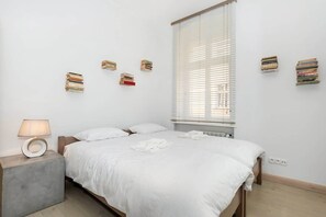A bedroom with twin beds side by side, dressed in white linens. There’s a small window and minimal décor, creating a peaceful atmosphere.