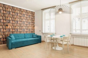  A cozy living room with a teal sofa positioned against a wall with a decorative brick pattern. The room is minimal but stylish, with a touch of color.