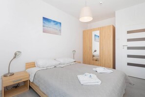 One bedroom with a double bed on which there is a grey bedspread. Next to it are bedside tables and a wardrobe.