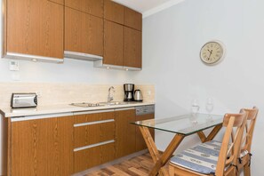 The kitchenette is equipped with wooden cabinets, a compact dining table with two wooden chairs, and essential appliances like a kettle and stove. The space is functional and neatly organized.