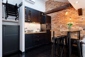 A modern kitchen with dark cabinetry, accented by a rustic exposed brick wall. The countertop has a few decorative plants, adding freshness to the design.