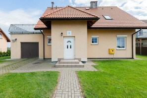 The exterior of a cozy, single-story house with a traditional red roof and a well-maintained lawn leading to the entrance.
