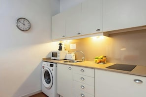 The fully equipped kitchen features modern appliances, including a microwave, toaster, coffee machine, and a four-burner electric stovetop. A washing machine is conveniently located in the corner of the kitchen, allowing for laundry to be done during your