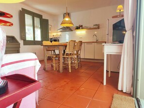 The open-plan living and dining area features a rustic wooden table surrounded by wicker chairs, perfect for enjoying meals together. The kitchen is equipped with modern appliances, including a coffee maker, a toaster, and a microwave, ensuring you have e