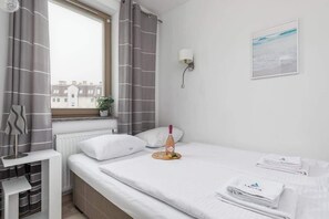 A cozy bedroom with a neatly made bed, gray bedding, and modern decor elements. A window lets in natural light.