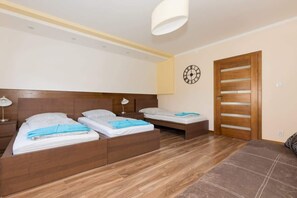 A view of the same bedroom showing the entrance next to which is a single bed next to which is a bedside table with a lamp and a double bed. 