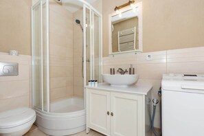 A small, well-lit bathroom with a toilet, sink, and beige tiles. Compact and functional design.