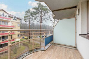 An outdoor balcony with wooden flooring, overlooking a residential area with lush greenery.