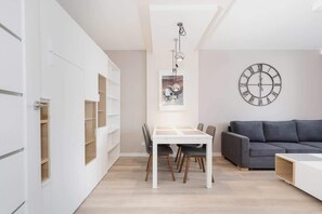 Another view of a living room with a wall clock, comfortable seating, and light decor, creating an inviting environment.