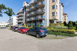 A multi-story residential building, possibly an apartment complex, with cars parked in front. It’s a sunny day, and there are some trees in the background.