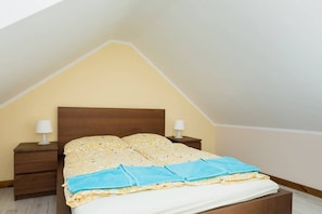 Cosy attic bedroom with double bed. There are tables with lamps on two sides of the bed. 