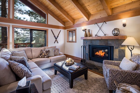 Great room has lofty beamed ceilings, gas fireplace, flat screen TV and deck