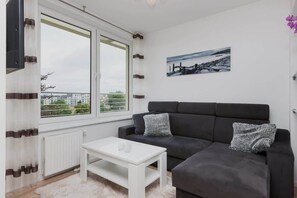 A spacious living room featuring a large sofa, coffee table, and minimalist decor with a balcony visible through glass doors.