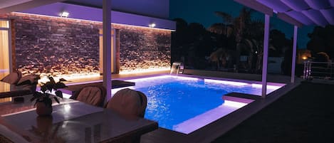 Zona piscina iluminada de noche con cascada y jacuzzi en marcha