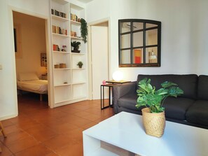 Comfortable grey sofa, a large arched mirror with a black frame and a white bookshelf with a few books and decorative items is visible in the background, adding a touch of personality to the room.  The spacious living room is ideal for relaxing and enjoyi
