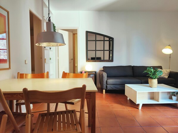 The spacious living room features a large, comfortable sofa, a coffee table with a potted plant and a modern, white coffee table with storage space, perfect for enjoying a relaxing evening.  The dining area features a large table and four chairs, offering