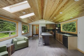 Kitchen w/ custom walnut cabinets, concrete island, and secluded forest views.