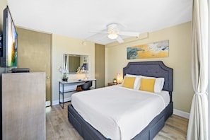 Bedroom with queen-size bed, ceiling fan, TV, dedicated workspace, and closet.