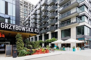 The modern facade of a residential building with large balconies and green landscaping around the entrance.