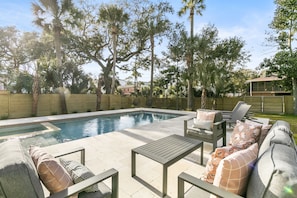 The fenced-in backyard features an outdoor living room and four pool loungers on ivory travertine decking to provide a relaxing respite after a long day at the beach.