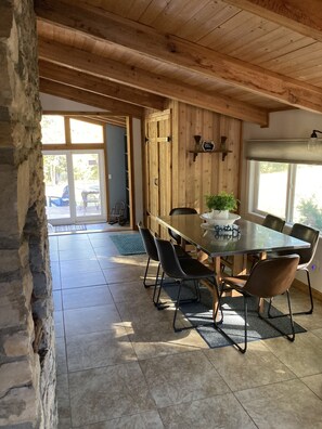 Dining room with stone wall and vaulted pine ceiling and huge picture windows.